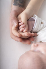 inquadratura sulle mani di papà, mamma e neonato.