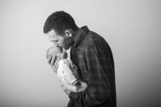 Neonato in braccio al papà, che lo bacia teneramente sulla fronte. foto in bw