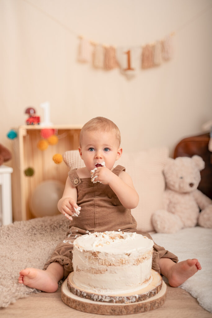 bimbo primo compleanno salopette velluto a coste marrone, torta semplice di panna, banner con numero 1 sullo sfondo